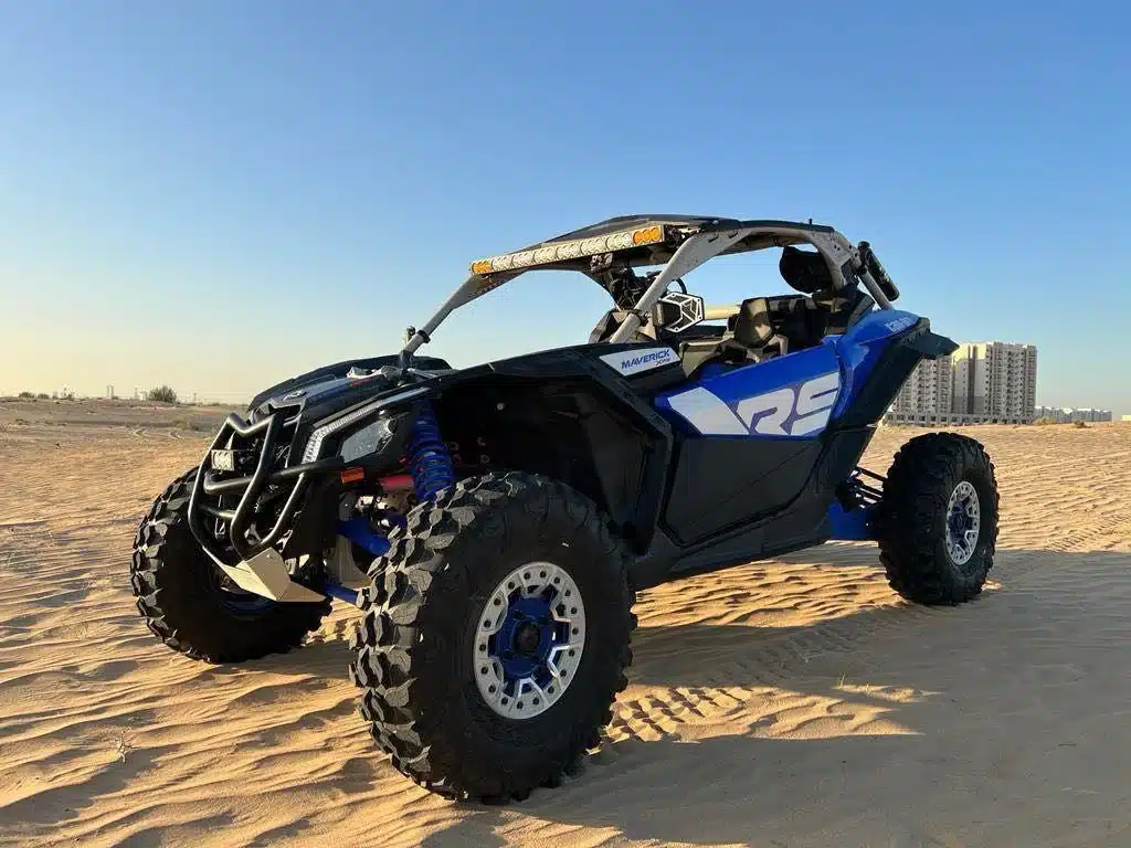 Can-Am Maverick X3 dune buggy parked on Dubai desert sand with blue sky background.